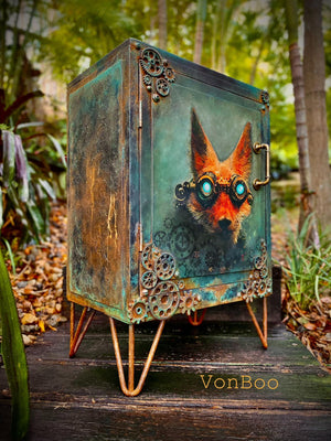 May include: A small, rusty green cabinet with a fox face painted on the front. The cabinet has a metal handle and is decorated with gears. The cabinet is sitting on four hairpin legs. The text 'VonBoo' is visible on the bottom right of the image.