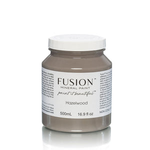 May include: A 500mL bottle of Fusion Mineral Paint in the color Hazelwood. The bottle is a light brown color and has a white lid. The label on the bottle says 'Fusion Mineral Paint paint it beautiful Hazelwood 500mL 16.9 fl oz'. The bottle is sitting on a white background.