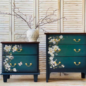 May include: Two teal blue nightstands with gold hardware and floral decals. The nightstands have two drawers each. The nightstands are sitting on a white wood floor.