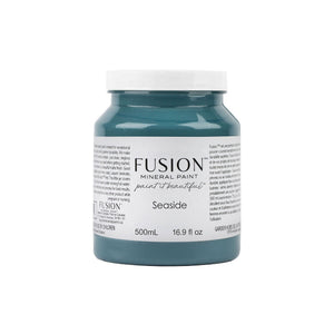 May include: A 500mL bottle of Fusion Mineral Paint in the color Seaside. The bottle is teal blue and has a white label with the Fusion logo and the words 'paint it beautiful' in a script font. The bottle is labeled with the color name Seaside and the size 500mL and 16.9 fl oz.